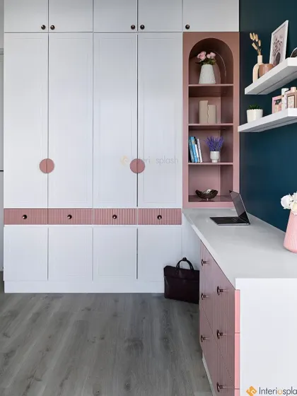 This contemporary bedroom features a floor-to-ceiling white wardrobe with blush pink accents. A built-in desk and a curved bookshelf are cleverly integrated into the unit for a multi-functional design.