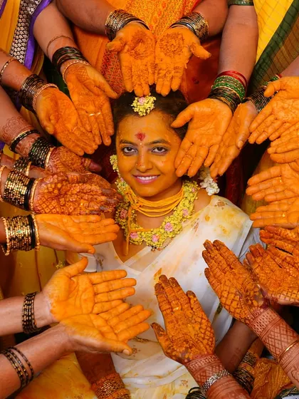 A vibrant haldi ceremony photo, where the bride's dark mehendi stain stands out beautifully against the yellow turmeric.
