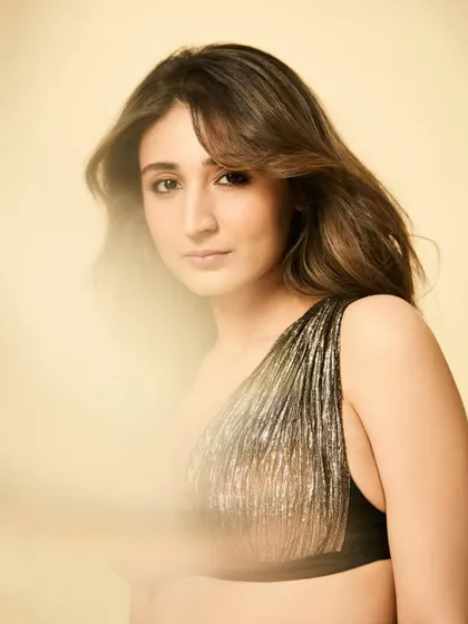 A dreamy, soft-focus portrait of Dhvani. The one-shoulder shimmer top is perfect for catching the light and creating an ethereal glow.