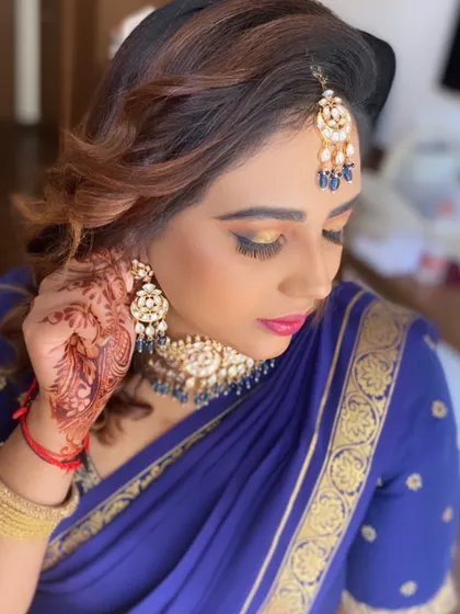 A stunning look with a bold blue saree. The makeup features dramatic, smoky eyes with a golden shimmer and a bright pink lip for a high-contrast, glamorous effect.