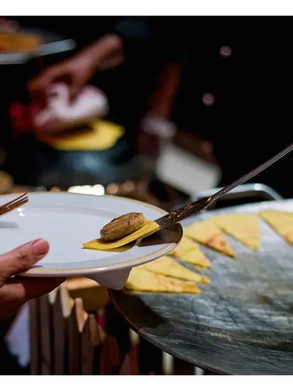 A guest being served a delicate gilauti kebab on a small, crisp bread base, fresh from the tawa.