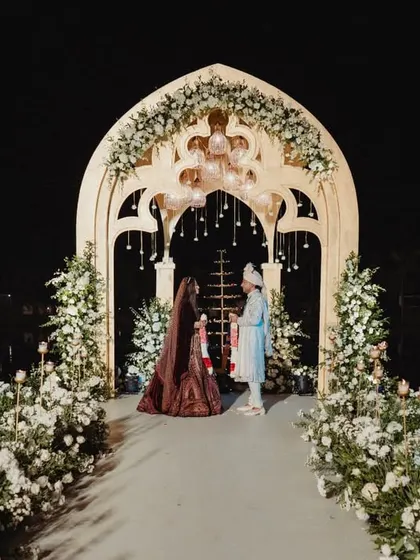 The couple shares a quiet moment on the Varmaala platform we built over the lagoon. The elegant archway, adorned with white flowers and hanging glass globes, creates a romantic frame against the dark water and night sky.