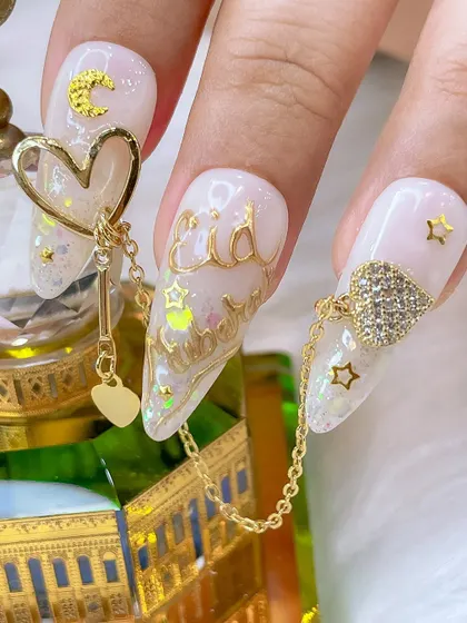 A close-up of the Eid nail art, highlighting the intricate details like the gold chain connecting two nails and the sparkling heart charm.