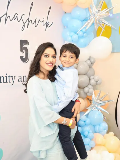 A mother holds her son, the birthday boy, for a photo in front of the party decorations.