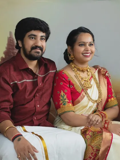 A beautifully composed portrait of a couple in traditional South Indian attire, seated against a backdrop of ancient temple ruins.