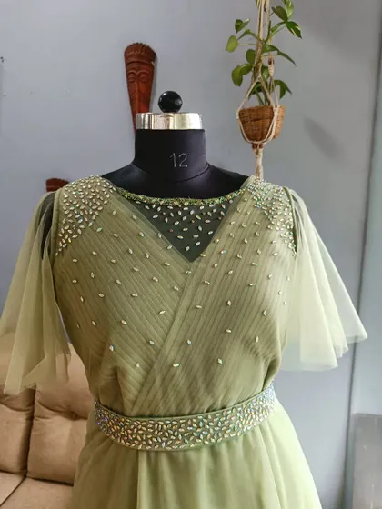 A detailed shot of the pleated and embellished bodice of the green gown. Notice the precise alignment of the pleats and the scattered beading that adds a subtle sparkle.