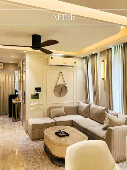 The "after" shot of a living room transformation, now a cozy and elegant space with a neutral L-shaped sofa, classic wall molding, and warm ambient lighting.