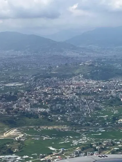 An aerial view of the Kathmandu Valley as we fly into Nepal. The landscape is a patchwork of towns and green fields, nestled between the hills.