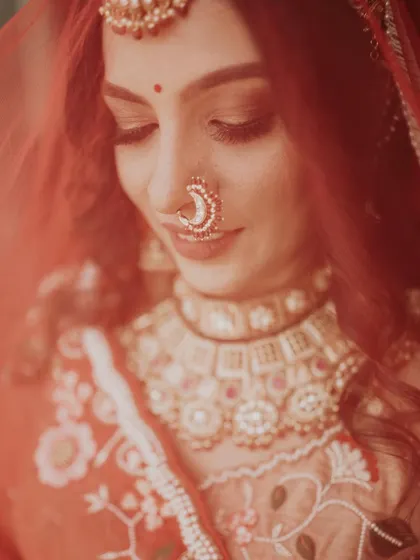 A close-up shot of the bride through her red veil. Her gentle smile and beautiful nose ring are the focus of this soft and romantic portrait.