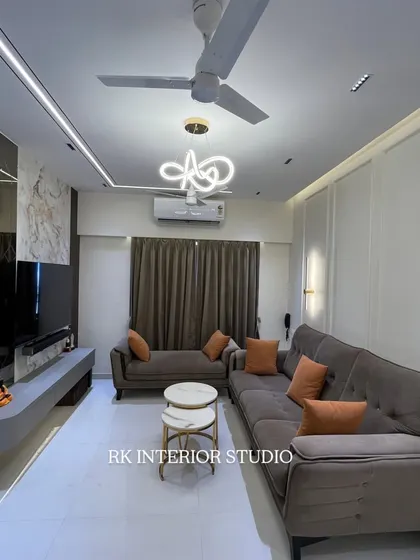 This living room features a floating TV unit with a marble-finish back panel and a mirrored wall that makes the space feel larger. The modern chandelier and profile lights in the ceiling add to the luxurious ambiance.