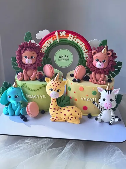 Double the fun with this jungle cake for twins. This design features two small cakes connected by a rainbow, with adorable, handcrafted safari animals like lions, elephants, and giraffes.