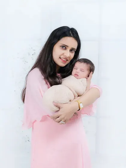 A mother in a soft pink dress holds her sleeping newborn close. The photo is gentle, serene, and full of love.