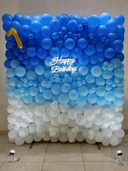 This ombre balloon wall creates a beautiful visual effect, transitioning from deep blue to light blue and finally to white. It's a versatile and impactful backdrop, here used for a first birthday, complete with a neon sign and a number one foil balloon.