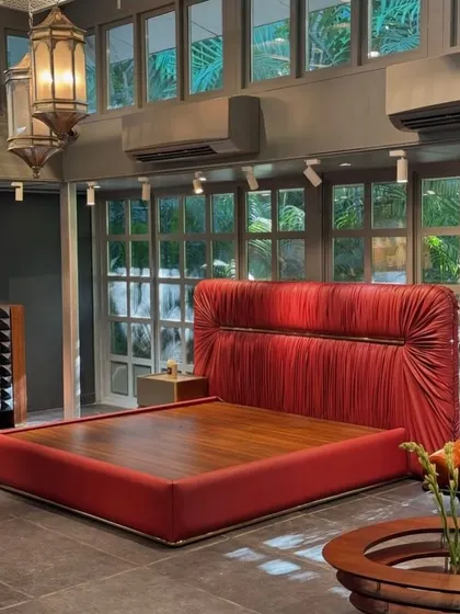 A bold statement in red. This bed features a dramatic, padded headboard with soft, sculptural drapery in a vibrant fabric, set in a modern showroom. This piece strikes an elegant balance between contemporary design and traditional craftsmanship.