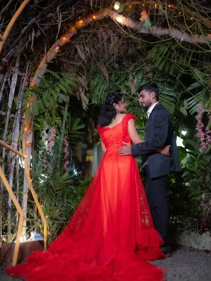 A magical evening pre-wedding photo of a couple under a garden arch adorned with fairy lights, creating a romantic and enchanting atmosphere.