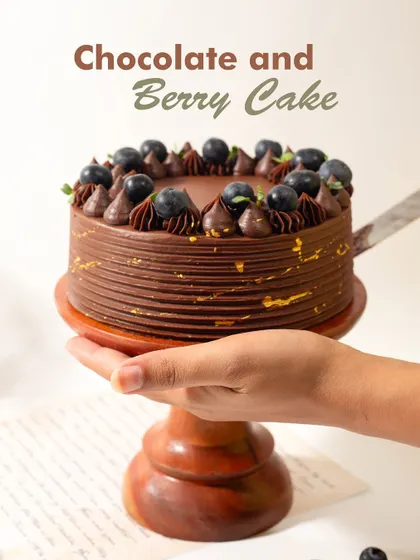 Our Chocolate and Berry Cake is a match made in dessert heaven. A hand holds up the cake, showcasing its elegant design and fresh berry topping.