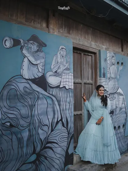 The bride poses playfully in front of a large, artistic mural, her smile as vibrant as the artwork behind her.