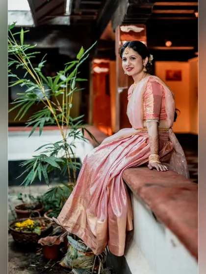 A graceful portrait of the bride-to-be seated on a ledge, her beautiful pink saree and the natural greenery creating a picturesque scene.