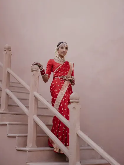 A graceful portrait of the bride in her red silk saree, descending the stairs of the palace. This shot has a timeless, classic feel, highlighting the elegance of the bride and the venue.