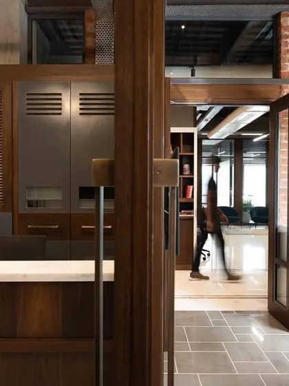 A glimpse of the reception area and entryway at the Prodigy Investment Management office. The design combines dark wood cabinetry with exposed brick and tiled flooring, creating a welcoming yet professional first impression.