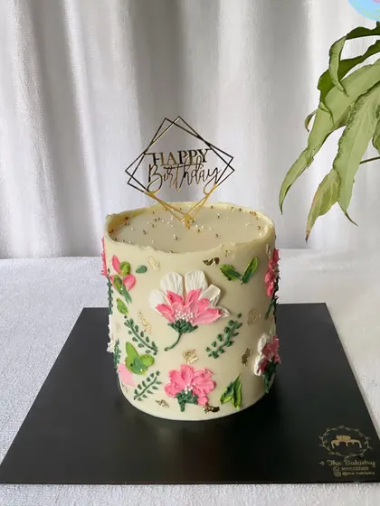 A beautifully hand-painted floral cake with a modern, artistic feel, topped with a geometric "Happy Birthday" topper.