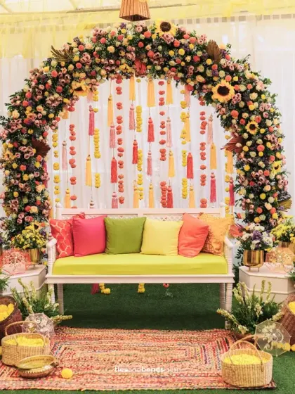 A vibrant Haldi seating area designed for celebration. The floral arch, colorful cushions, and hanging tassels create a picture-perfect spot for the couple.