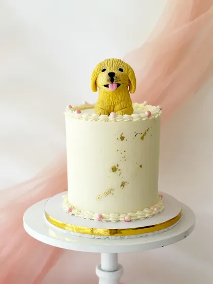 A cake for a dog lover, featuring a sculpted golden retriever popping out of the top. The simple buttercream cake is speckled with gold for a touch of sparkle.