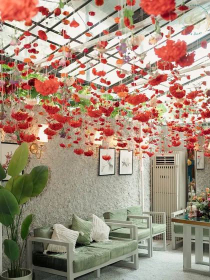 A lush Mehendi setup with a ceiling of floating red roses and comfortable green velvet seating. The contrast of colors and textures creates a rich and inviting atmosphere.