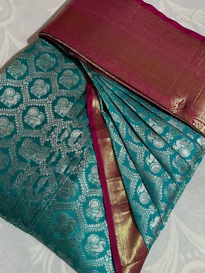 A teal blue saree with silver motifs and a pink border. It's now perfectly pleated and ready for any special occasion.
