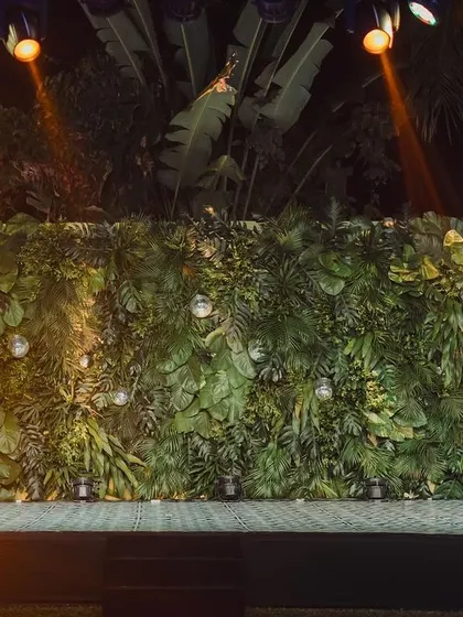 A lush green foliage wall serves as a natural yet dramatic DJ backdrop for this "Disco Jungle" themed party, punctuated by spotlights.