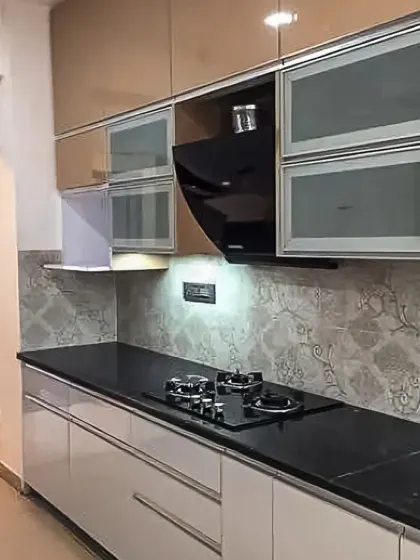 This kitchen pairs beige and white cabinets with a patterned backsplash and a sleek black chimney hood, creating a modern and elegant look.