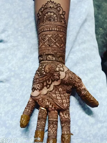 A single hand showing a full, traditional mehendi design. The pattern is dense and covers the entire hand and arm with classic motifs.