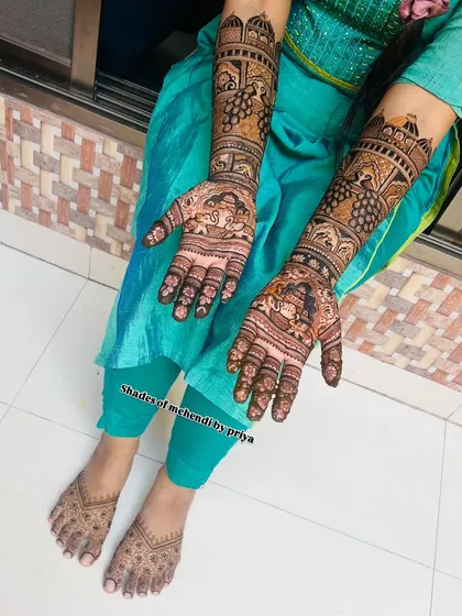 A top-down view of the engagement mehendi, showing the detailed work on both arms and feet. The designs feature traditional motifs like peacocks and elephants.