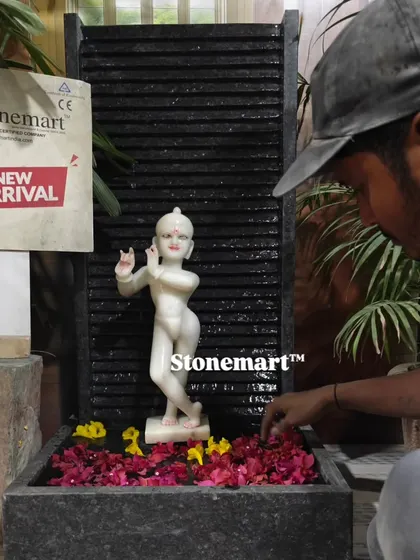 An artisan carefully adds flower petals to the water of the Kanha Ji fountain, preparing it for display.