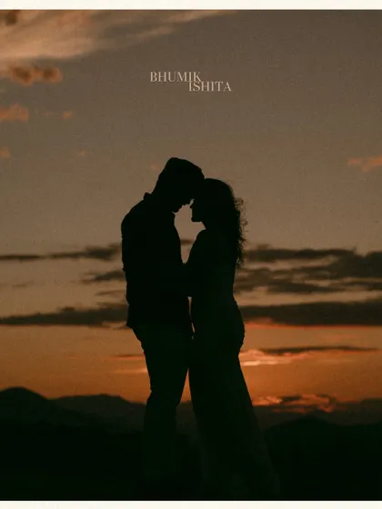 A classic sunset silhouette in the Georgian mountains. The couple is framed against the warm, orange sky, creating a simple, beautiful, and deeply romantic pre-wedding image.
