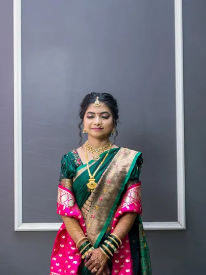 A full-length portrait of the bride against a simple background, allowing her stunning green and pink saree to take center stage.