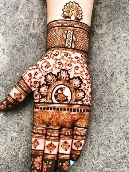 A unique design featuring a peacock as the centerpiece on the back of the hand. The fingers are decorated with geometric patterns, and a smaller peacock motif sits gracefully on the wrist.