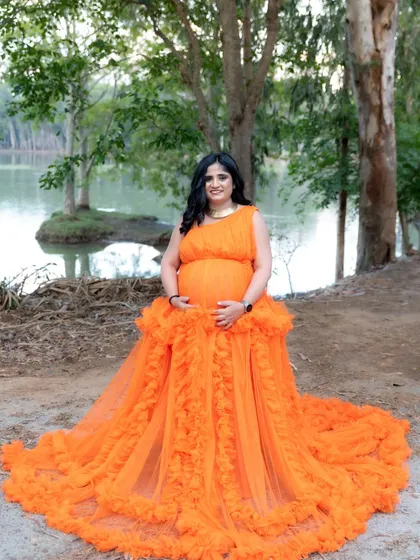 A lovely lakeside portrait of a mom-to-be in a vibrant orange gown. The calm water and trees in the background create a peaceful and natural atmosphere.