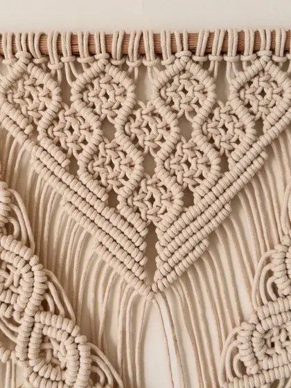 A close-up of the intricate diamond knot pattern from a classic off-white macrame wall hanging.