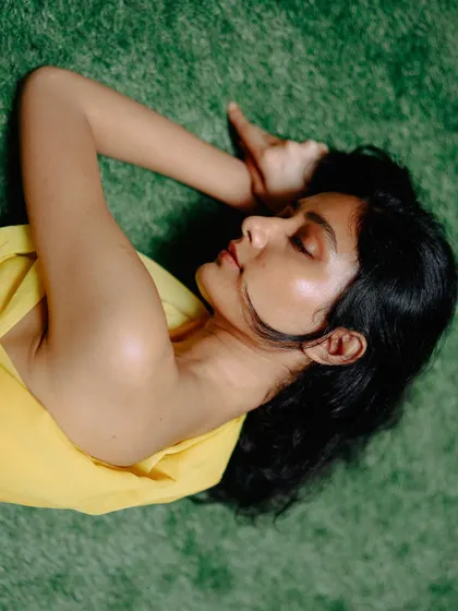 An overhead shot of a model in yellow fabric lying on green turf. The color contrast and serene pose create a visually striking and peaceful image.