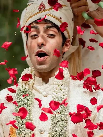 A groom's joyful reaction as he is showered with red rose petals during the 'baraat' or wedding procession.