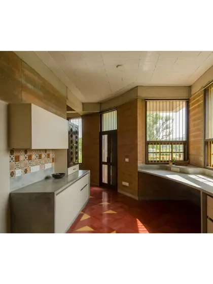 The kitchen in the "Breathe" house features rammed earth walls and cement countertops. The design prioritizes natural light and ventilation, with large windows and a simple, functional layout that complements the home's eco-sensitive philosophy.