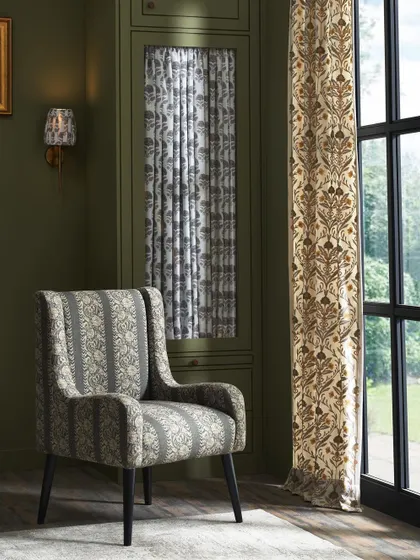 This image highlights an upholstered armchair and matching curtains within a classic interior. The focus is on how the fabric's pattern and texture interact with the light from the window, adding elegance to the space.