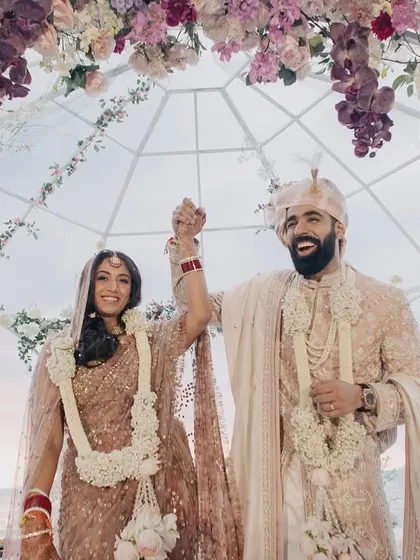 The triumphant and joyous exit of the couple after their wedding ceremony. Their happy expressions and raised hands tell a story of pure celebration.
