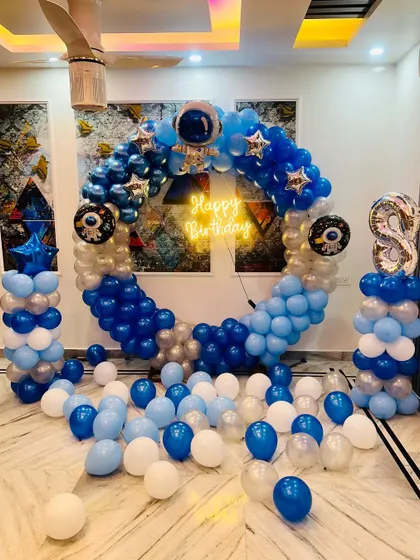 A space-themed birthday decoration designed for a home living room. A large circular balloon arch in blue and silver creates a focal point, complete with astronaut and planet details.