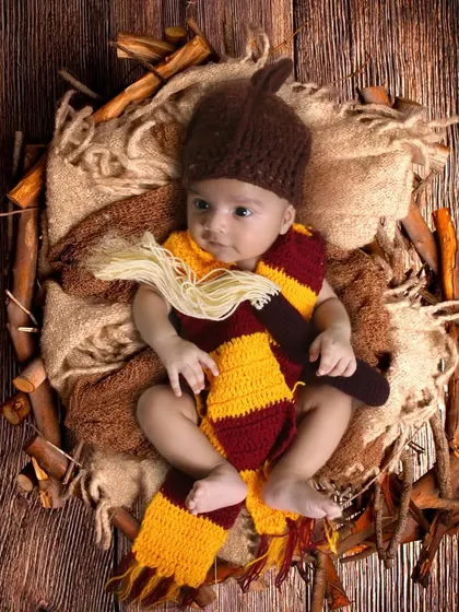 A newborn dressed in a Harry Potter scarf and hat, ready for their journey to Hogwarts.