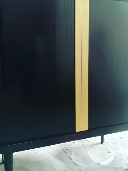 A console table being finished in our workshop. This piece has a black finish with gold accent strips and tambour-style rolling doors for a retro-modern look.