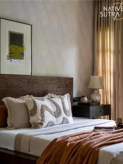 A beautifully styled rustic modern bedroom. The dark wood bed frame is complemented by an earthy orange throw and patterned cushions, while the abstract art adds a contemporary touch against the textured wallpaper.