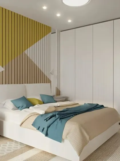 This bedroom features a geometric accent wall with yellow, wood, and white panels. The simple white bed and floor-to-ceiling wardrobe complete this fresh and modern look.
