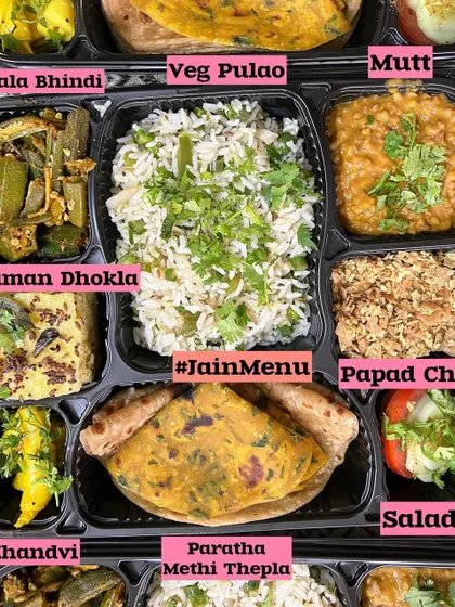 A delicious and wholesome Jain meal box. This thali includes Veg Pulao, Masala Bhindi, Khaman Dhokla, Khandvi, and a Methi Thepla, offering a wonderful variety of flavors.